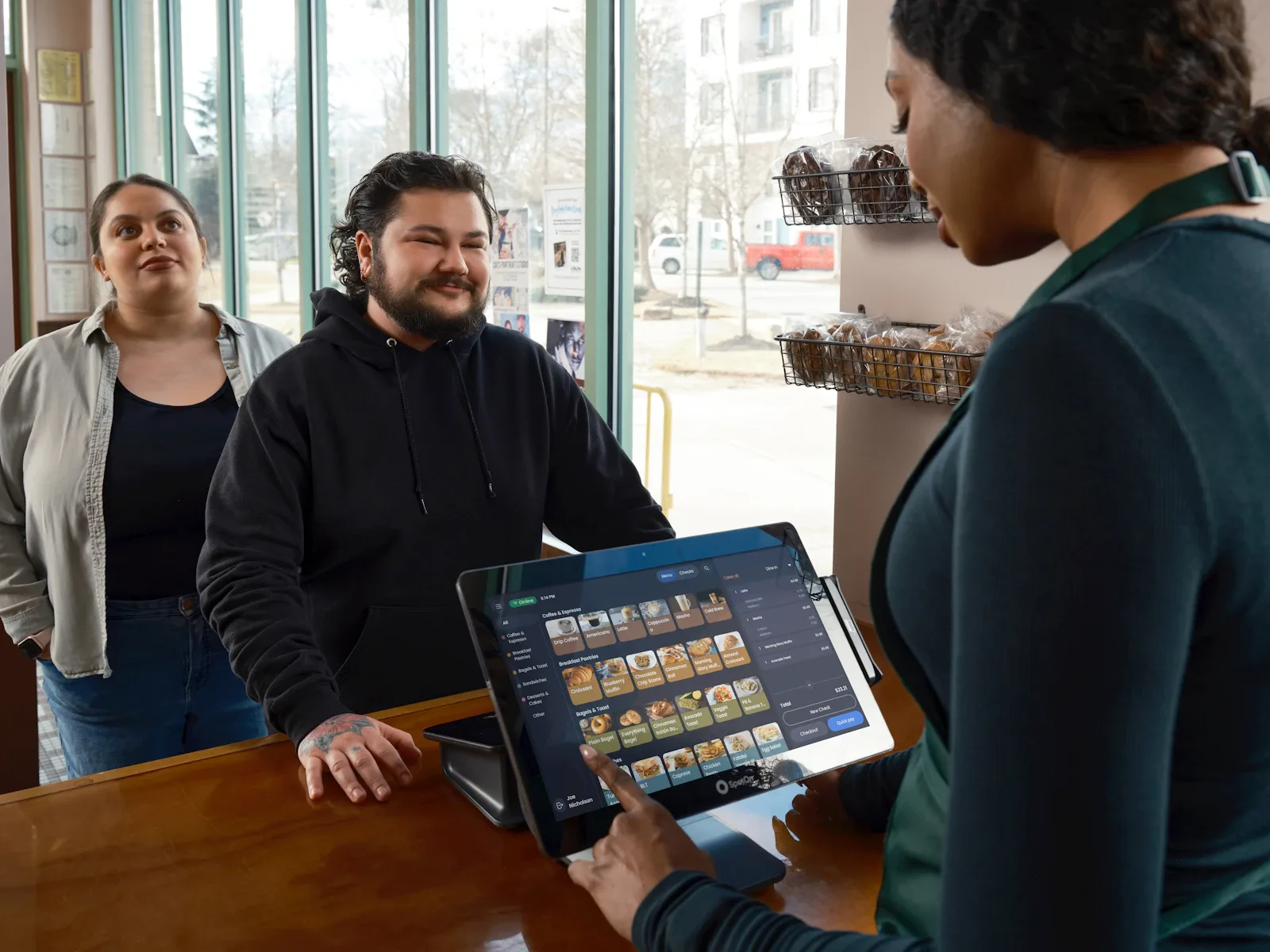 Restaurant staff at the counter showing a tablet to customers placing their order
